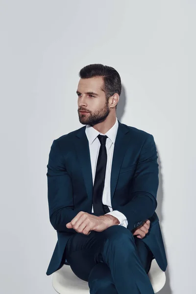 Quiet contemplation. Handsome young man looking away while sitting against grey background — Stock Photo, Image