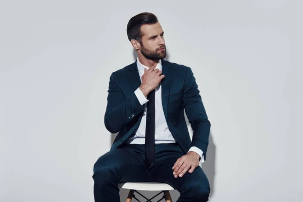 Tired. Handsome young man pulling his collar while sitting against grey background — Stock Photo, Image