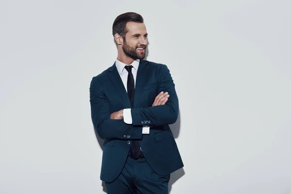 Un hombre de negocios guapo. Encantador joven que mantiene los brazos cruzados y sonriendo mientras está de pie sobre un fondo gris —  Fotos de Stock