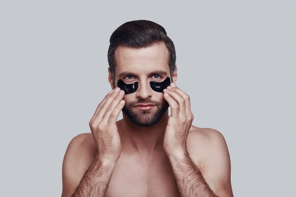 Personal care. Handsome young man applying medical eye patch while standing against grey background — Stock Photo, Image