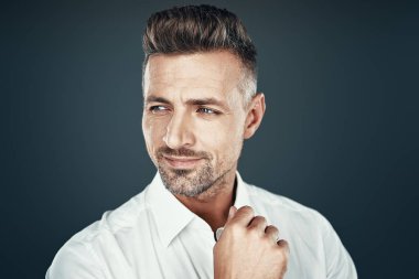 Güven ve karizma. Yakışıklı genç adam gülümseyerek ve gri arka plan karşı dururken uzağa bakıyor