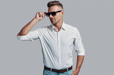 Modern maço. Yakışıklı genç adam gülümseyen ve gri arka plan karşı dururken güneş gözlüğü ayarlama