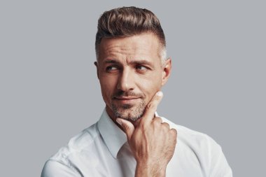 Bir cevap bulmaya çalışıyorum. Yakışıklı genç adam gri arka plan karşı ayakta iken uzağa bakıyor ve gülümsüyor