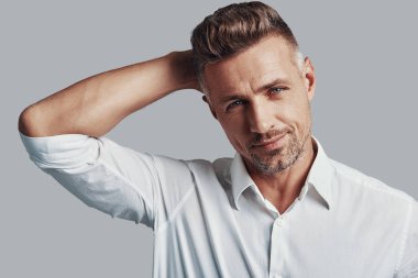 Gerçek maço. Yakışıklı genç adam kameraya bakıyor ve gri arka planda dururken gülümsüyor