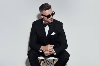 Mükemmel bir görünüm. Gri arka plan aleyhine otururken uzakta bakan tam takım elbise ve papyon Charming genç adam