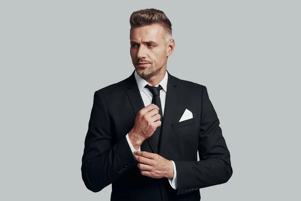 Confident in his style. Handsome young man adjusting his sleeve while standing against grey background — Stock Photo, Image