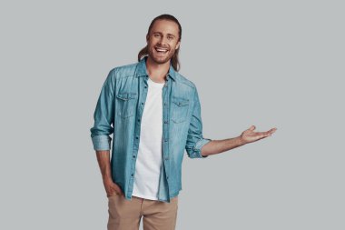 Şuraya bak! Yakışıklı genç adam kopya alanı işaret ve gri arka plan karşı dururken gülümseyerek