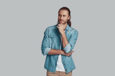 Düşünü? Yakışıklı genç adam gri arka plan karşı dururken uzağa bakıyor ve tutmak ve çene üzerinde