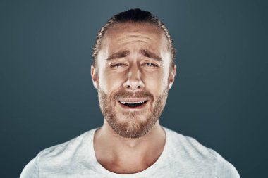 Bugün senin günün değil. Sinirli genç adam kameraya bakıyor ve gri arka plan aleyhine dururken bir yüz yapıyor