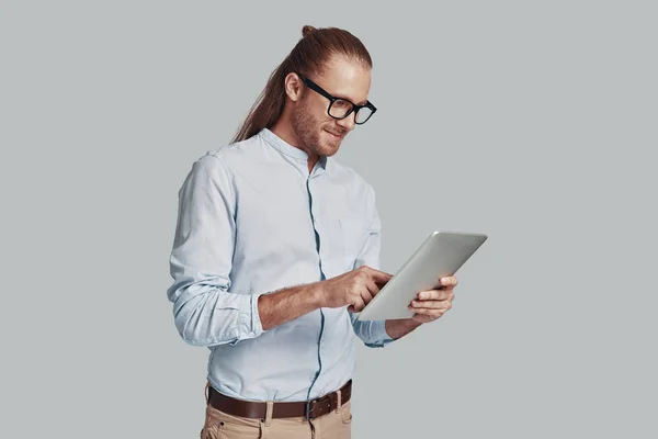 신선한 아이디어를 찾고 있습니다. 잘 생긴 젊은 남자 작업 노트북을 사용 하 여 하 고 회색 배경에 대 한 서 있는 동안 미소 — 스톡 사진