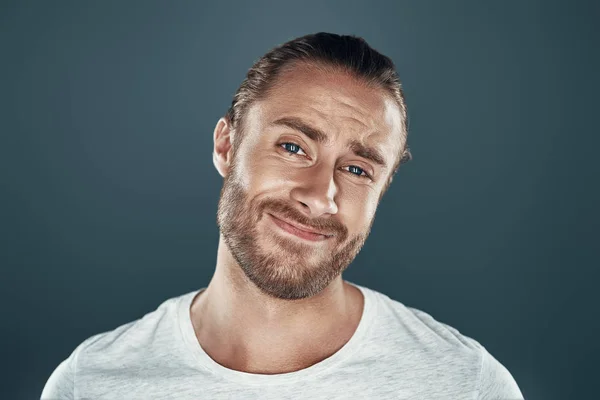 Cerco di continuare a sorridere. Bello giovane uomo guardando la fotocamera e facendo un volto mentre in piedi contro sfondo grigio — Foto Stock