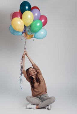 Eğlenceli. Çekici genç kadın balonları tutan ve gri arka plan karşı uçarken gülümseyen