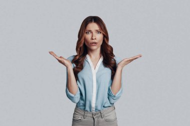 Belirsiz -lik. Gri arka plan aleyhine dururken akıllı rahat giyim genç kadın bir yüz yapma ve gesturing