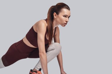 Kazanmaya kararlı. Gri arka plana karşı egzersiz yaparken esneme çekici genç kadın