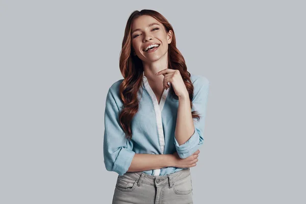 Sonrisa sincera. Atractiva joven mujer mirando a la cámara y sonriendo mientras está de pie sobre un fondo gris — Foto de Stock