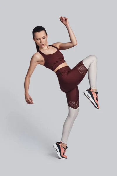 Βρείτε την ισορροπία σας! Πλήρες μήκος της ελκυστική νεαρή γυναίκα σε αθλήματα ρούχα άλμα κατά την άσκηση σε γκρίζο φόντο — Φωτογραφία Αρχείου