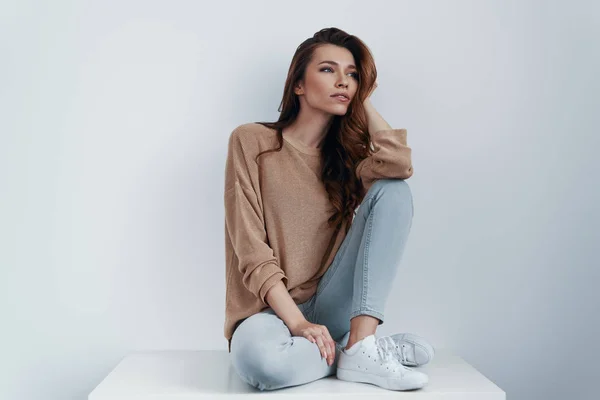 Day dreaming. Thoughtful young woman looking away while sitting against grey background — Stock Photo, Image