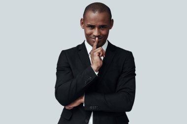 Herkesin bir sırrı vardır. Gri arka plan aleyhine dururken dudaklarında parmak tutan formalgiyim genç Afrikalı adam