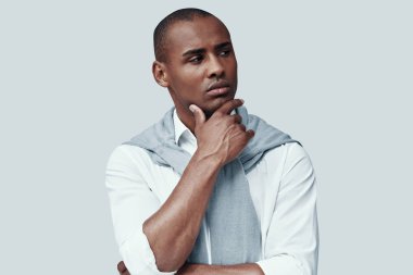 Derin düşünce. Yakışıklı genç Afrikalı adam uzağa bakıyor ve gri arka plan aleyhine dururken çene üzerinde el tutmak