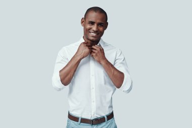 Büyüleyici. Yakışıklı genç Afrikalı adam kameraya bakıyor ve gri arka plan aleyhine dururken gülümsüyor