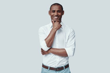 Samimi bir gülümseme. Yakışıklı genç Afrikalı adam kameraya bakıyor ve gri arka plan aleyhine dururken gülümsüyor