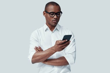 Her zaman kullanılabilir. Yakışıklı genç Afrikalı adam gri arka plan karşı dururken akıllı telefon kullanarak