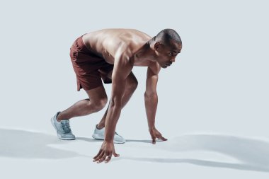 Çok zorluyor. Gri arka plan aleyhine egzersiz yaparken başlangıç çizgisinde duran spor giyim genç Afrikalı adam tam uzunlukta