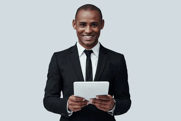 O negócio é a vida dele. Encantador jovem africano em formalwear trabalhando usando tablet digital enquanto está de pé contra fundo cinza — Fotografia de Stock