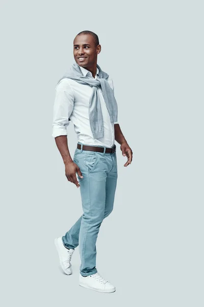 Με αυτοπεποίθηση και ομορφιά. Πλήρες μήκος του νεαρού Αφρικανό άντρα που κοιτάζει μακριά και χαμογελά ενώ στέκεται ενάντια στο γκρίζο φόντο — Φωτογραφία Αρχείου