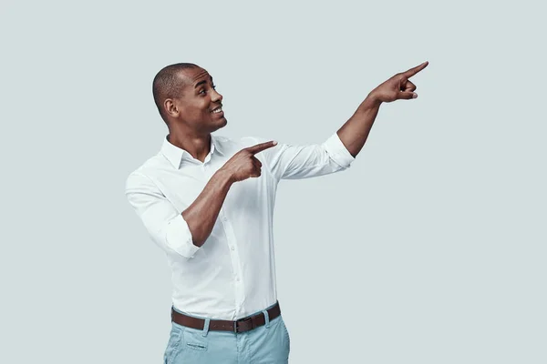 Take a look! Handsome young African man pointing copy space and smiling while standing against grey background