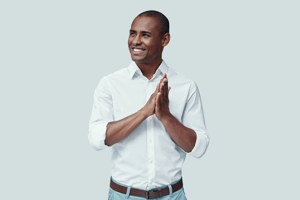 Herzensbrecher. schöner junger afrikanischer Mann, der wegschaut und lächelt, während er vor grauem Hintergrund steht — Stockfoto