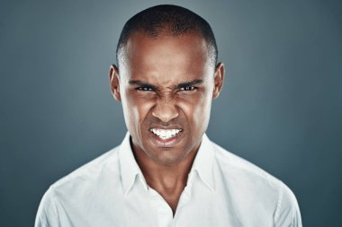 Sinirleniyorum. Gri arka plan aleyhine dururken kameraya bakan ve kaşlarını çatarak gömlekli genç Afrikalı adam memnun değil