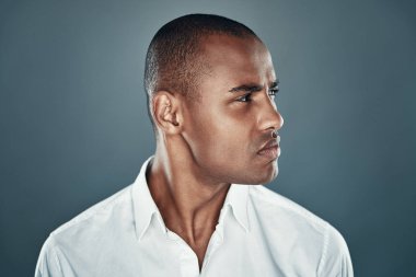 Kendinden emin bir görünüm. Gri arka plan aleyhine dururken gömlek yakışıklı genç Afrikalı adam uzağa bakıyor