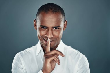 Bir sırrım var. Gri arka plan aleyhine dururken gömlek yakışıklı genç Afrikalı adam kameraya bakıyor ve dudaklarında parmak tutmak