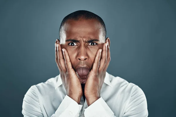 Bad news. Shocked young African man in shirt looking at camera and making a face while standing against grey background