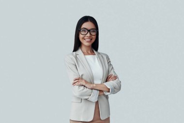 Genç ve zeki. Çekici genç Asyalı kadın gri arka plan karşı dururken kameraya bakıyor