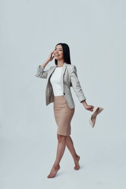 Kolay adım. Çekici genç Asyalı kadın telefonda konuşurken ve gri arka plan karşı dururken yüksek topuklu taşıyan tam uzunlukta