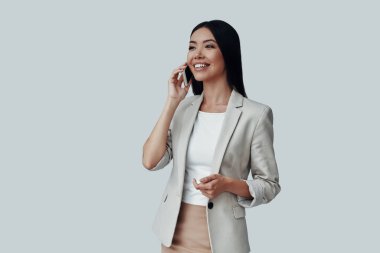 Güzel konuşma. Çekici genç Asyalı kadın telefonda konuşurken ve gri arka plan karşı dururken gülümseyerek
