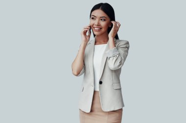 Her zaman kullanılabilir. Çekici genç Asyalı kadın telefonda konuşurken ve gri arka plan karşı dururken gülümseyerek