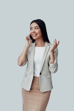 Sohbet etmek. Çekici genç Asyalı kadın telefonda konuşurken ve gri arka plan karşı dururken gülümseyerek