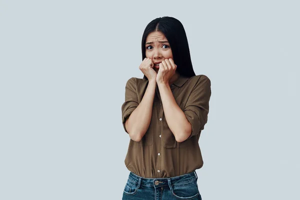 Worried. Confused young Asian woman making a face while standing against grey background — Stock Photo, Image