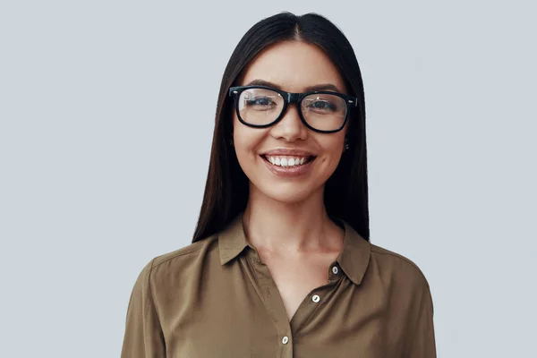 Inteligencia. Atractiva joven mujer asiática mirando a la cámara y sonriendo mientras está de pie sobre fondo gris —  Fotos de Stock