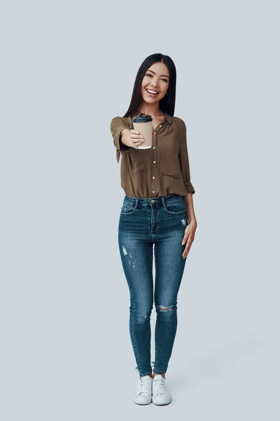¿Quieres? Longitud completa de atractiva joven mujer asiática mirando a la cámara y sonriendo mientras está de pie sobre fondo gris —  Fotos de Stock