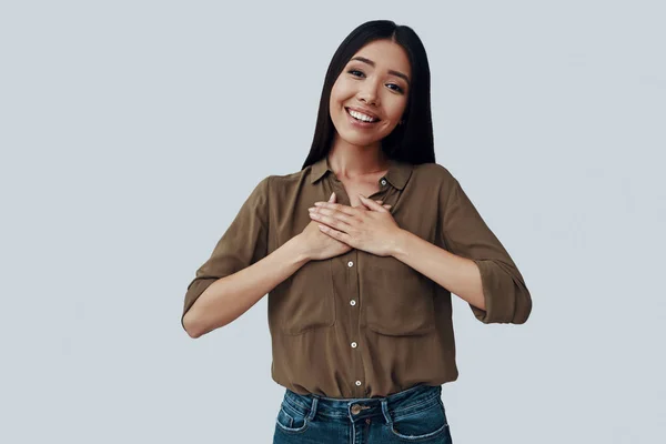 Con todo mi corazón. Atractiva joven mujer asiática mirando a la cámara y sonriendo mientras está de pie sobre fondo gris —  Fotos de Stock