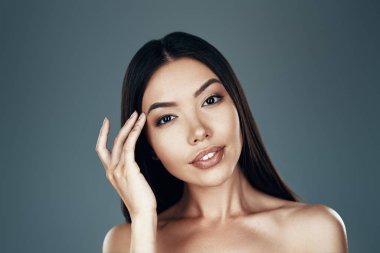 Özgür ve rahat hissediyorum. Gri arka planda dururken kameraya bakan güzel genç Asyalı kadın