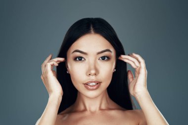 Flört özne güzellik. Gri arka planda dururken kameraya bakan güzel genç Asyalı kadın