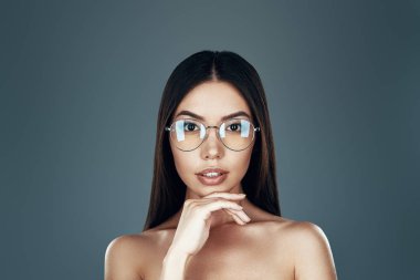 Mükemmel bir stil. Gri arka planda dururken kameraya bakan güzel genç Asyalı kadın