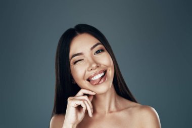 Zahmetsiz güzellik. Güzel genç Asyalı kadın kameraya bakıyor ve gri arka planda dururken gülümsüyor