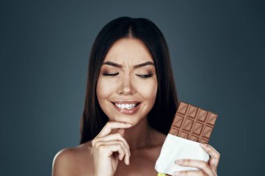 Yemeden önce düşün. Gri arka planda dururken bir yüz yapma güzel genç Asyalı kadın