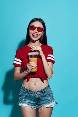 Mükemmel bir ferahlık. Mavi arka plan aleyhine dururken gülümseyen çekici genç Asyalı kadın